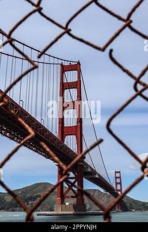 Ein vertikales Bild der berühmten Golden Gate Bridge in San Francisco, Kalifornien, sichtbar durch einen alten, rostigen Zaun von Fort Point Stockfoto