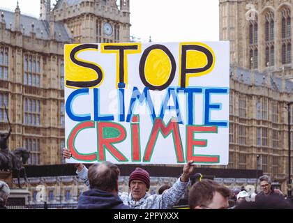 Man hält das Protestplakat "Stop Climate Crime" vor Westminster am Earth Day, Extinction Rebellion Protest Weekend, London, 2023. April. Stockfoto