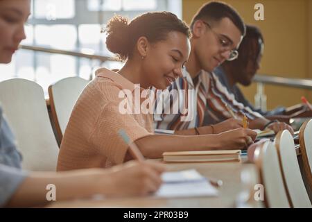 Gruppe von Schülern, die beim Vortrag in einer Reihe sitzen und Notizen in Notizbüchern machen Stockfoto