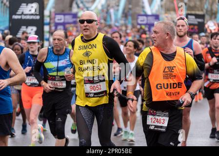 Blinder Läufer nimmt am TCS London Marathon 2023 Teil, der Tower Hill, London, UK, durchquert. Simon Goodall mit Reiseleiter Kevin Borley Stockfoto