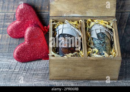 Glasbecher mit Blumentee und Glasbecher mit Kiefernkonfitüre in einer hölzernen Geschenkbox und zwei rote Herzen auf einem Tisch, Nahaufnahme. Wunderschönes Geschenk für Stockfoto