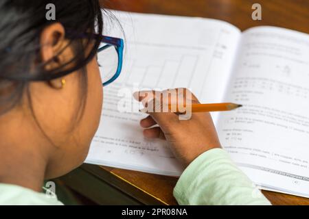 Ein Mädchen im Alter von 9 Jahren schreibt mit einem Bleistift auf ein Buch