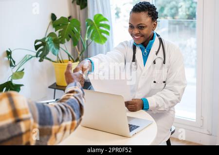 Junge Ärztin schüttelt sich die Hand mit dem Patienten, nachdem sie die Ergebnisse ihrer Untersuchungen vorgelegt hat. Konzept: Medizin, Krankheit, Gesundheitsversorgung Stockfoto