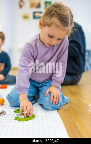 Ein kleines Mädchen, das mit Plasticin spielt. Sensorische Entwicklung und Erfahrungen, thematische Aktivitäten mit Kindern, Entwicklung der Feinmotorik Stockfoto