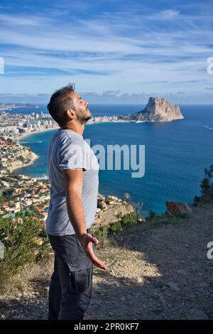 Ein lächelnder Wanderer, der den blauen Himmel betrachtet und tief einatmet, feiert die Freiheit des Meeresbodens bei Erreichen des Gipfels. Positive Emotionen, Erfolg f Stockfoto