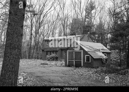 Ein verwittertes und verlassenes Haus und eine Garage mit Plane, die das undichte Dach entlang der historischen Battle Road an einem bedeckten Frühlingstag in Minutem bedeckt Stockfoto