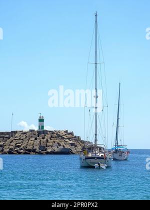 Yachten in der Bucht nahe dem Ufer mit einem Leuchtturm an einem sonnigen Tag Stockfoto