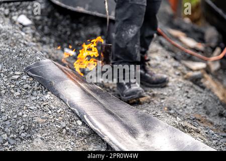 Erhitzen des Asphalts mit einer Flamme. Abdichtung des Fundaments und der Wände des Hauses Stockfoto