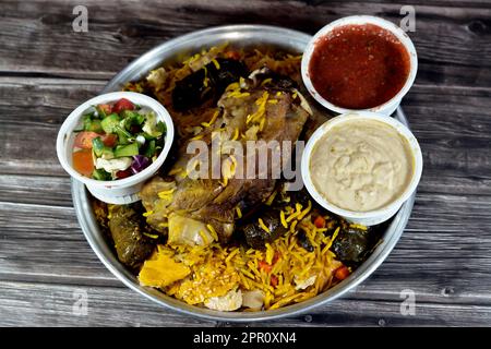 Ein gut gekochter Lammschaft mit gelbem Basmati-Reis und gemischtem Gemüse und gefüllten Traubenblättern Mahshi Mahshy mit weißem Reis, der im OV geröstet wird Stockfoto