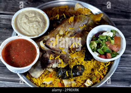 Ein gut gekochter Lammschaft mit gelbem Basmati-Reis und gemischtem Gemüse und gefüllten Traubenblättern Mahshi Mahshy mit weißem Reis, der im OV geröstet wird Stockfoto