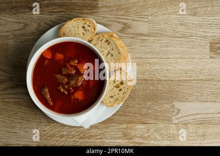 Traditionelle ungarische Gulaschsuppe mit Brot auf einem Holztisch. Großer Blickwinkel Stockfoto
