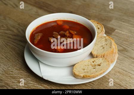 Traditionelle ungarische Gulaschsuppe mit Brot auf einem Holztisch Stockfoto