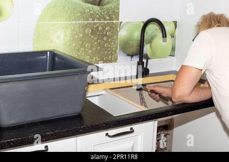 Installation von Sanitäranlagen und Waschbecken in der Küche. Der Mann repariert den Wasserhahn. Stockfoto