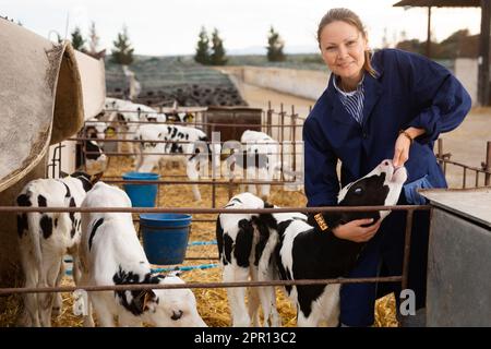 Lächelnde Farmerin, die mit dem kleinen Kalb im offenen Stand spielt Stockfoto