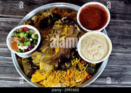 Ein gut gekochter Lammschaft mit gelbem Basmati-Reis und gemischtem Gemüse und gefüllten Traubenblättern Mahshi Mahshy mit weißem Reis, der im OV geröstet wird Stockfoto