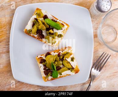 Scheiben getoastetes Brot mit Frischkäse, eingelegte Oliven und sonnengetrocknete Tomaten Stockfoto