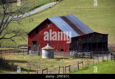 Rot, Holzverbot, mit Rostdach aus Zinn, auf einem großen Feld. Die Landstraße verläuft hinter uns. Das rostende Silo aus Zinnkorn sitzt im Scheunenhof. Stockfoto