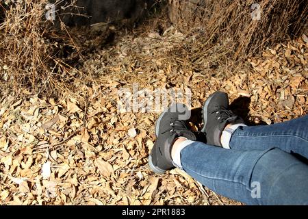 Beine einer Frau mit Jeanshosen und schwarzen Wanderstiefeln, die allein im Wald spaziert, als Teil des sozialen Problems des Verschwindens und des ungelegenen Wohnsitzes Stockfoto