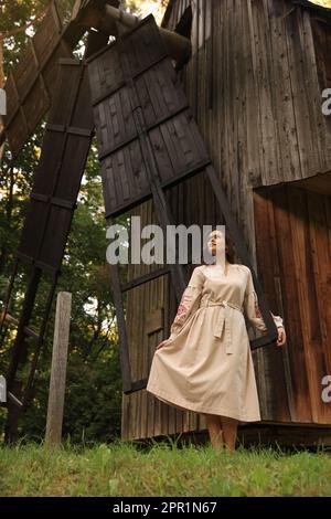 Eine schöne Frau, die ein gesticktes Kleid in der Nähe einer alten Holzmühle auf dem Land trägt. Ukrainische Nationalkleidung Stockfoto