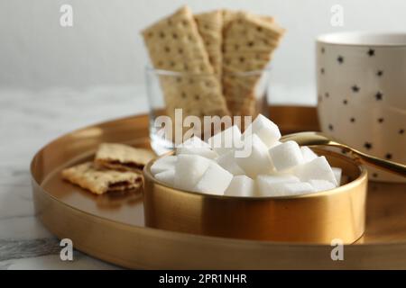 Raffinierte Zuckerwürfel in der Schüssel und aromatischer Tee auf weißem Marmortisch, Nahaufnahme Stockfoto