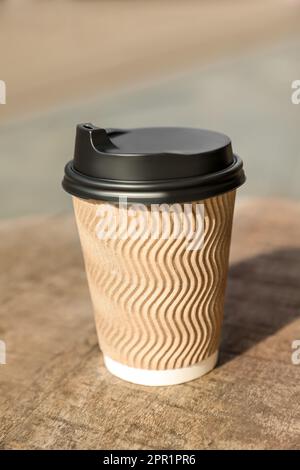 Kaffeetasse zum Mitnehmen aus Karton mit Kunststoffdeckel auf einem Holztisch in der Stadt Stockfoto