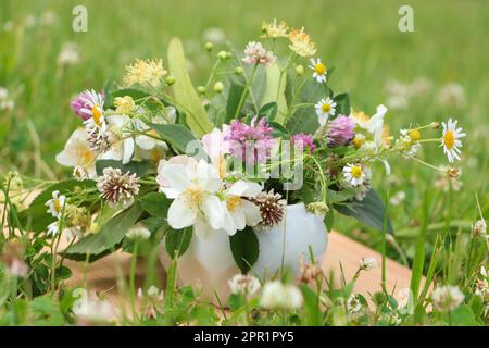 Keramikmörtel mit verschiedenen Wildblumen und Kräutern auf Holzbrettern auf der Wiese Stockfoto