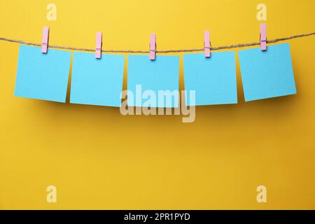 Holzkleidekabinen mit leeren Notizzetteln auf Garn vor gelbem Hintergrund. Platz für Text Stockfoto