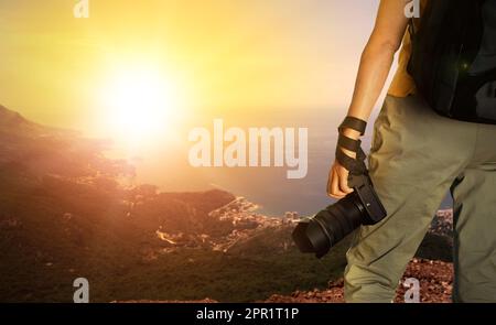 Fotograf mit professioneller Kamera und wunderschöner Blick auf Berge und Meer bei Sonnenuntergang im Hintergrund, Platz für Text Stockfoto