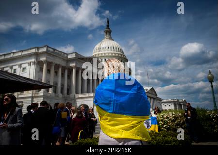 Washington, Vereinigte Staaten. 25. April 2023. Eine Frau wird vor einer ukrainischen Siegesauflösung während einer Pressekonferenz im US-Kapitol in Washington, DC, am Dienstag, den 25. April 2023 in die ukrainische Nationalflagge gewickelt. Kredit: Rod Lamkey/CNP/dpa/Alamy Live News Stockfoto