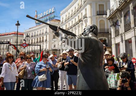 Madrid, Spanien. 25. April 2023. Eine Statue von König Juan Carlos I. mit einem Jagdgewehr, das auf die Statue des Bären und den Erdbeerbaum zeigt, während Dutzende Zuschauer zusehen, hinter dem traditionellen Tio Pepe Schild. Der chilenische Künstler Nicolás Miranda installierte eine Statue von König Juan Carlos mit einem Gewehr, um die Figur des Königs und seine Vorliebe für die Jagd nach gefährdeten Tieren zu verspotten. Kredit: SOPA Images Limited/Alamy Live News Stockfoto