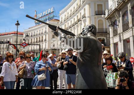 Madrid, Spanien. 25. April 2023. Eine Statue von König Juan Carlos I. mit einem Jagdgewehr, das auf die Statue des Bären und den Erdbeerbaum zeigt, während Dutzende Zuschauer zusehen, hinter dem traditionellen Tio Pepe Schild. Der chilenische Künstler Nicolás Miranda installierte eine Statue von König Juan Carlos mit einem Gewehr, um die Figur des Königs und seine Vorliebe für die Jagd nach gefährdeten Tieren zu verspotten. (Foto: David Canales/SOPA Images/Sipa USA) Guthaben: SIPA USA/Alamy Live News Stockfoto