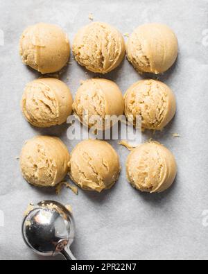 Schaufeln mit Vanille-Keksteig auf einem mit Pergament ausgekleideten Keksblatt, einfacher Vanille-Keksteig, der gleich gebacken wird Stockfoto