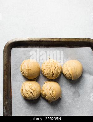 Schaufeln mit Vanille-Keksteig auf einem mit Pergament ausgekleideten Keksblatt, einfacher Vanille-Keksteig, der gleich gebacken wird Stockfoto