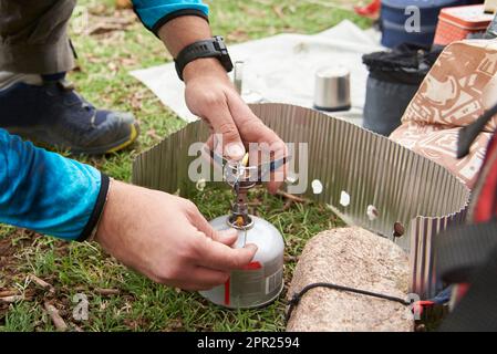 Ein unbekannter Mann, der einen Lagerofen anzündet, um auf einem Campingplatz zu kochen. Konzepte: Rucksackreisen, Camping-Lebensstil. Stockfoto