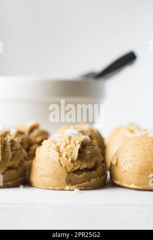 Schaufeln mit Vanille-Keksteig auf einem mit Pergament ausgekleideten Tablett, einfacher Vanille-Keksteig mit Salzflocken, die gebacken werden sollen Stockfoto