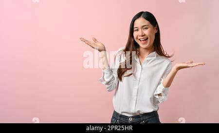 Junge, wunderschöne Asiatin, die ein weißes Hemd trägt und die Hände zur Seite zeigt auf pinkfarbenen, isolierten Hintergrund. Stockfoto