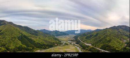 Panoramablick aus der Vogelperspektive auf dramatische Wolken über dem ländlichen Dorf im Tal bei Sonnenuntergang Stockfoto