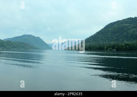 Wellen auf der Oberfläche eines großen Sees hoch in den Bergen, überwuchert mit dichten Nadelwäldern unter einem wolkigen Sommerhimmel. Teletskoye Lake, Altai, Stockfoto