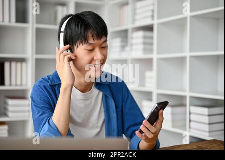 Fröhlicher junger Student, der gerne mit dem Smartphone Musik hört. Stockfoto