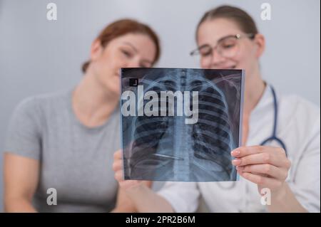 Der Arzt konsultiert eine kaukasische Frau und kommentiert die Röntgenaufnahme der Lunge. Stockfoto
