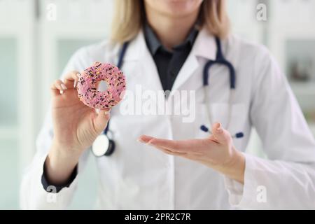 Der Ernährungsberater hält frischen Donut mit rosafarbenem Glasur in der Hand Stockfoto