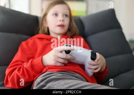 Fokussiertes Schulmädchen spielt Videospiele im Sessel Stockfoto