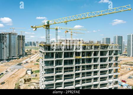 Kräne bauen neue Wohnhäuser auf einer Baustelle am blauen Himmel. Nahaufnahme aus der Luft. Stockfoto