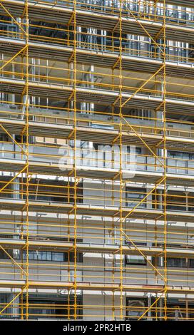 Gelbes Gerüst umgibt ein unvollendetes mehrstöckiges Gebäude, das das geometrische Design des Gebäudes unterstreicht Stockfoto