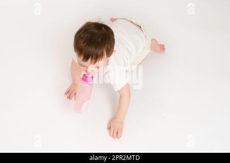 Happy Baby trinkt Milch aus der Flasche auf weißem Studiohintergrund. Ruhendes Kind isst Formel. Kind etwa zwei Jahre alt (ein Jahr neun Monate) Stockfoto