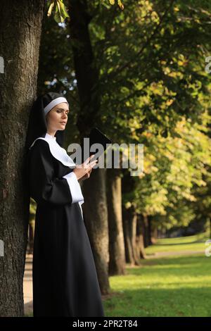 Junge Nonne, die an sonnigen Tagen im Park Bibel liest. Platz für Text Stockfoto