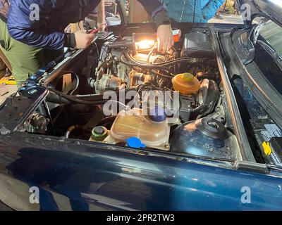 Der Werkstattmeister repariert ein Auto unter der Haube in einer Werkstatt in einer Garage. Stockfoto