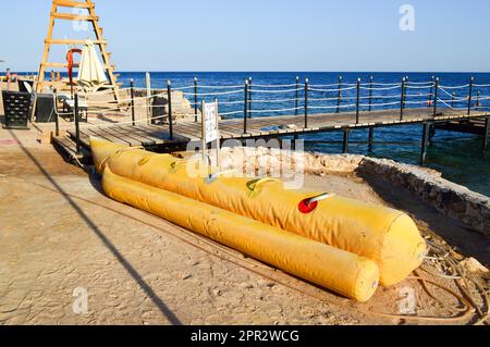 Aufblasbares gelbes Boot in Form einer Banane für die Unterhaltung von Touristen liegt am Strand in der Nähe des Piers im tropischen Meeressort in Ägypten Stockfoto