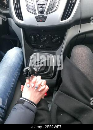 Mann und Frau, Mädchen, verliebtes Paar, Händchen halten mit ansehnlichen Händen in einem Auto mit mechanischem 6-Gang-Getriebe. Stockfoto