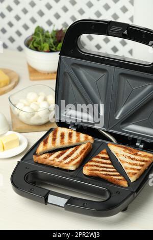 Moderner Sandwichmaker mit Brotscheiben auf weißem Tisch Stockfoto